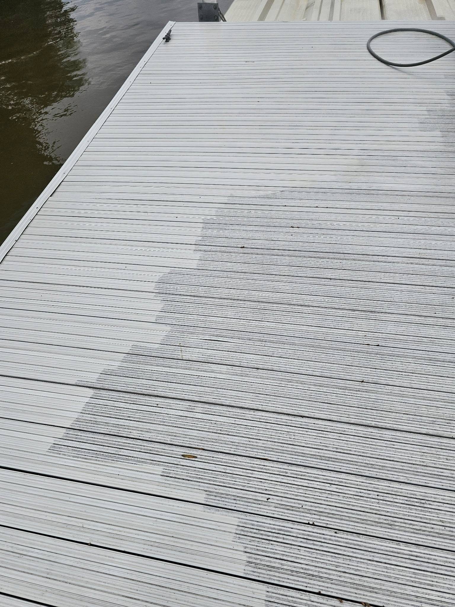 Composite dock decking mid-clean, showing a clear line between dirty and freshly washed boards